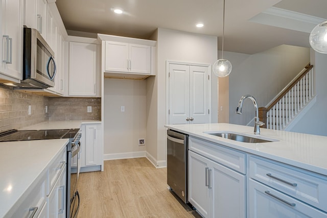 kitchen with appliances with stainless steel finishes, a sink, white cabinets, light wood-style floors, and tasteful backsplash