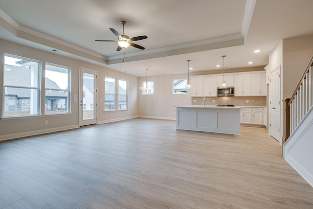 unfurnished living room featuring ornamental molding, a raised ceiling, a ceiling fan, stairs, and plenty of natural light