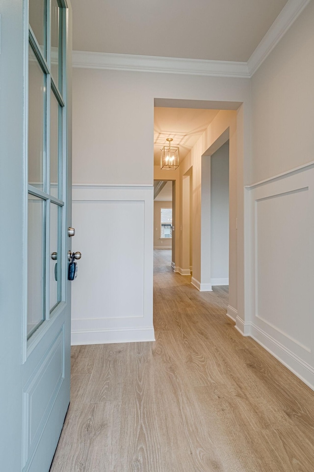 entrance foyer featuring a chandelier, light wood-type flooring, ornamental molding, a decorative wall, and wainscoting