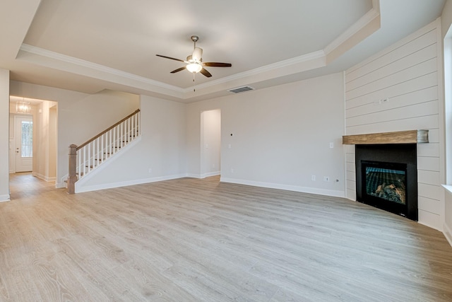 unfurnished living room with a tray ceiling, ornamental molding, stairway, ceiling fan, and light wood-type flooring