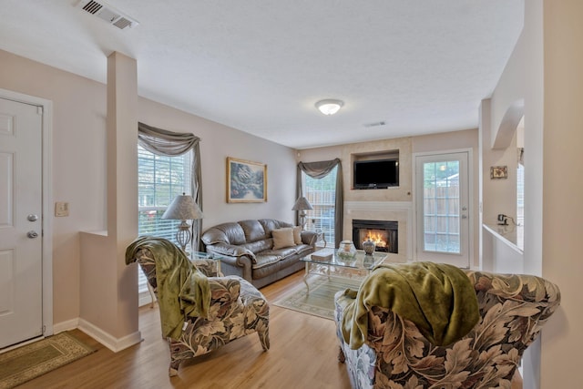 living room with visible vents, baseboards, a glass covered fireplace, and light wood-type flooring