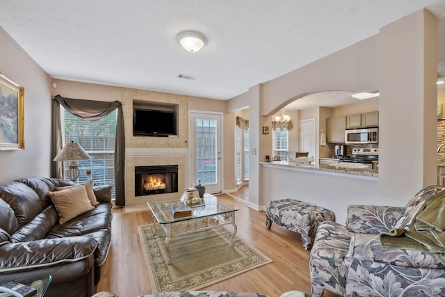 living area with visible vents, arched walkways, a large fireplace, a notable chandelier, and light wood-style floors