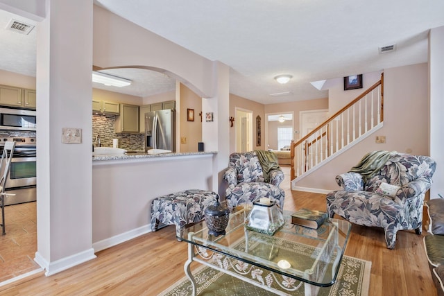 dining area featuring stairway, arched walkways, light wood-style flooring, and visible vents