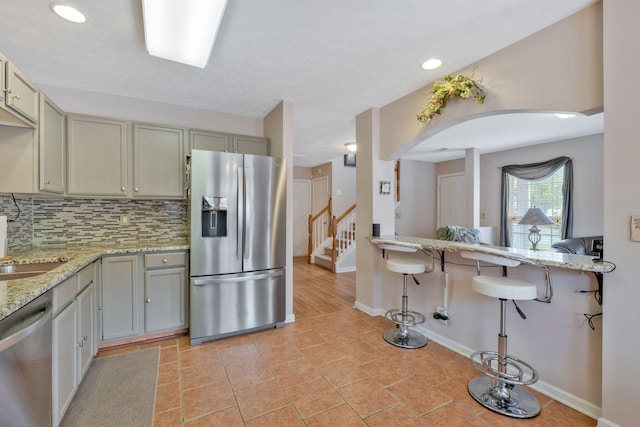 kitchen featuring arched walkways, tasteful backsplash, light stone countertops, baseboards, and stainless steel appliances