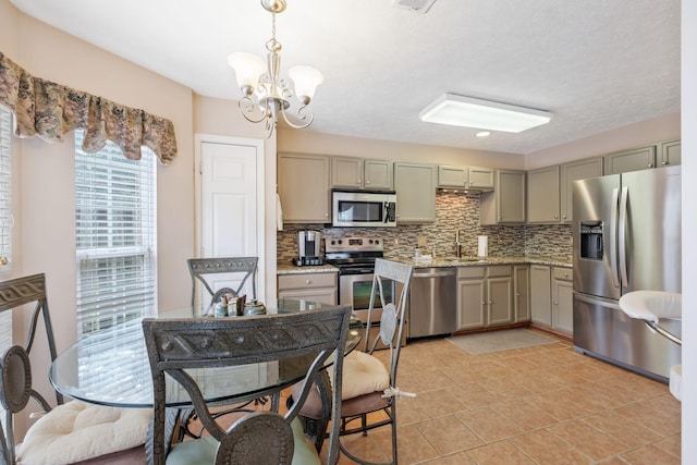 kitchen featuring a notable chandelier, appliances with stainless steel finishes, light stone counters, backsplash, and gray cabinetry