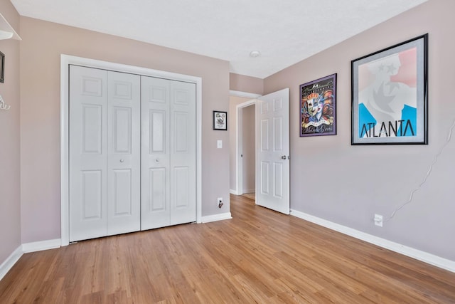 unfurnished bedroom featuring baseboards, light wood finished floors, and a closet