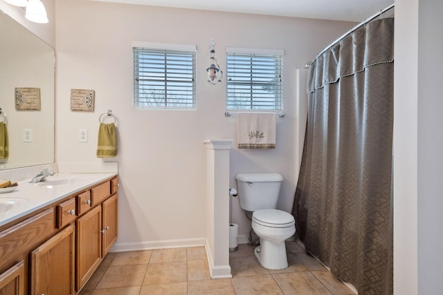 bathroom with double vanity, tile patterned flooring, a sink, baseboards, and toilet