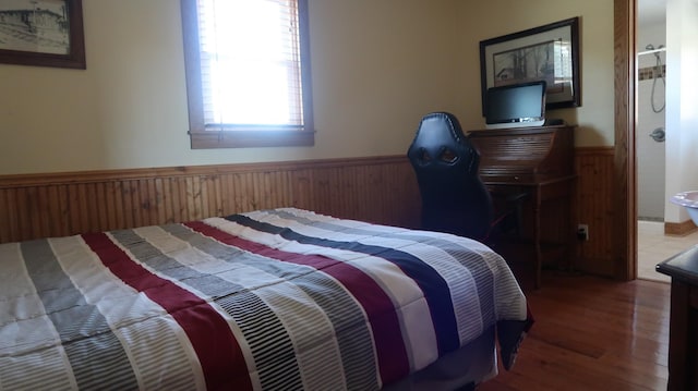 bedroom with wainscoting, wood walls, and wood finished floors
