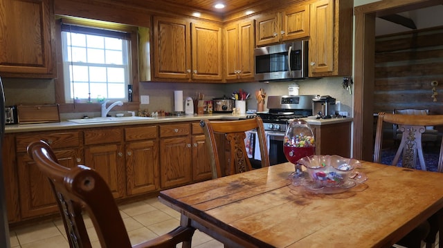 kitchen with brown cabinets, light tile patterned floors, stainless steel appliances, and a sink