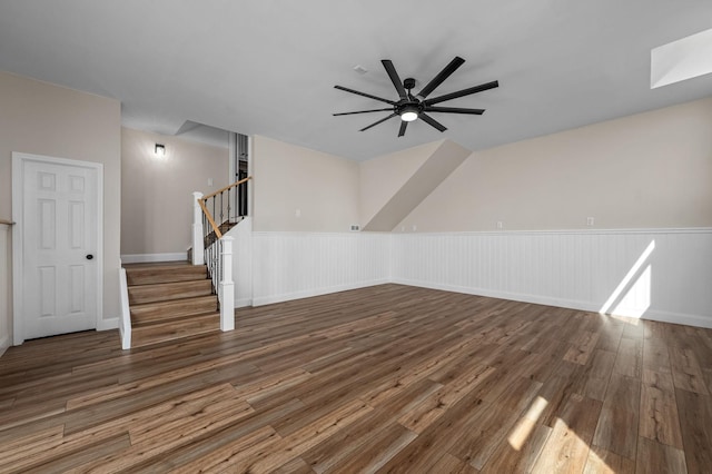 additional living space with a wainscoted wall, a skylight, stairs, wood finished floors, and a ceiling fan