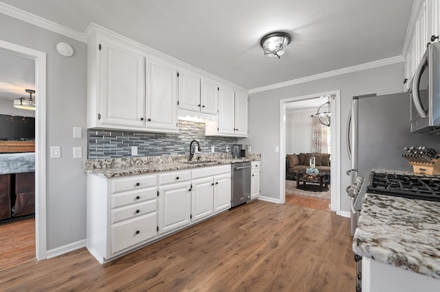 kitchen featuring crown molding, wood finished floors, appliances with stainless steel finishes, white cabinetry, and a sink