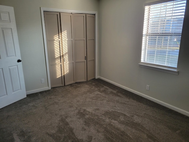 unfurnished bedroom featuring a closet, baseboards, and dark colored carpet