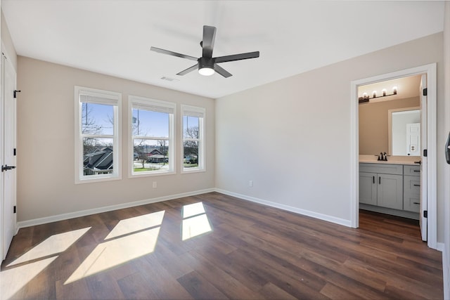 unfurnished bedroom featuring dark wood-style flooring, baseboards, a sink, connected bathroom, and a ceiling fan