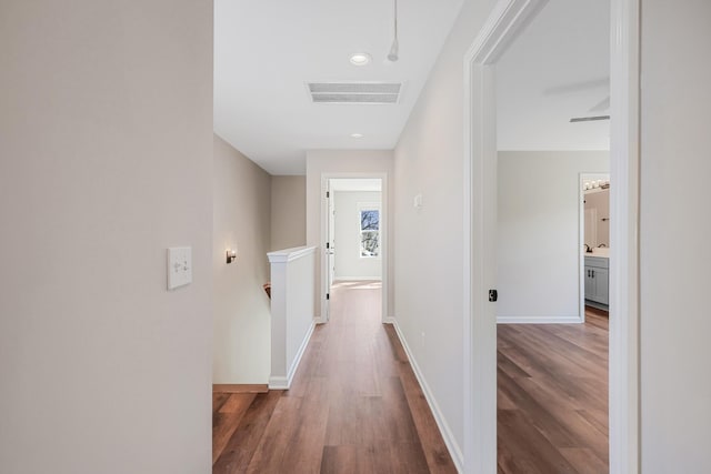 hallway featuring wood finished floors, an upstairs landing, baseboards, and visible vents