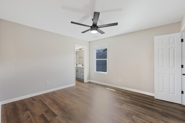 unfurnished bedroom featuring dark wood finished floors, baseboards, ensuite bath, and a ceiling fan