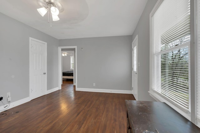interior space featuring a ceiling fan, dark wood-type flooring, and baseboards