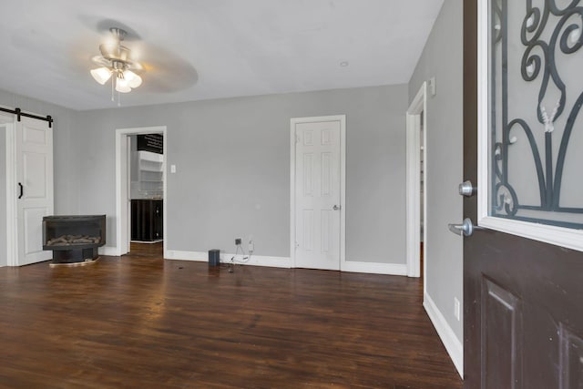 living area with baseboards, a barn door, ceiling fan, and wood finished floors