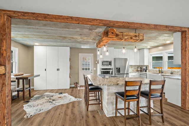 kitchen featuring white cabinetry, wood finished floors, decorative backsplash, and stainless steel appliances