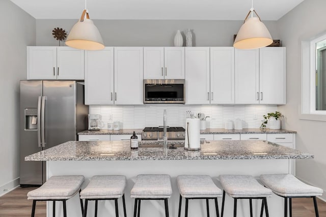 kitchen with backsplash, hanging light fixtures, light stone countertops, and appliances with stainless steel finishes