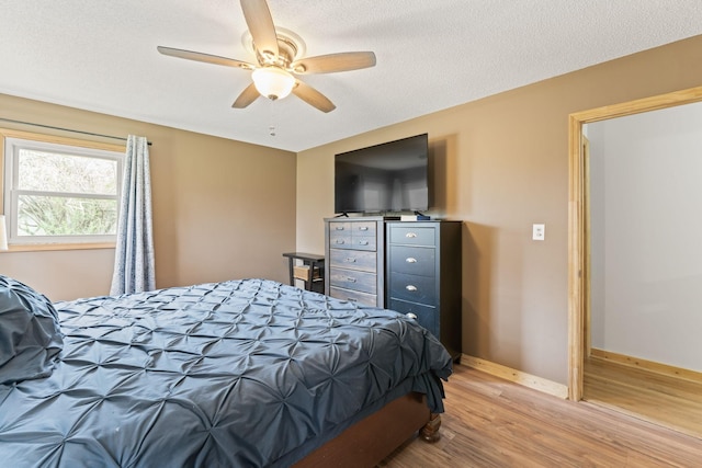 bedroom featuring baseboards, light wood-type flooring, ceiling fan, and a textured ceiling