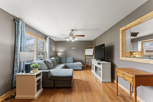 living room with a textured ceiling, baseboards, light wood finished floors, and ceiling fan