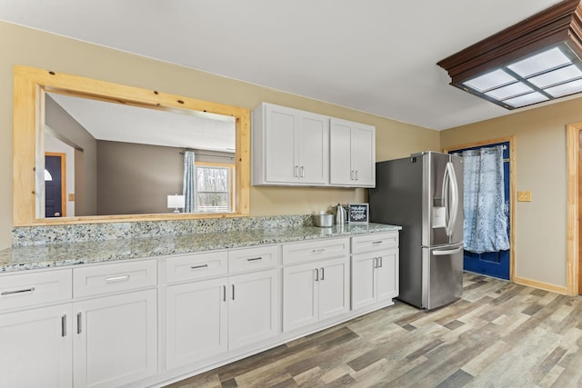 kitchen featuring white cabinets, light wood-style flooring, stainless steel refrigerator with ice dispenser, and light stone countertops