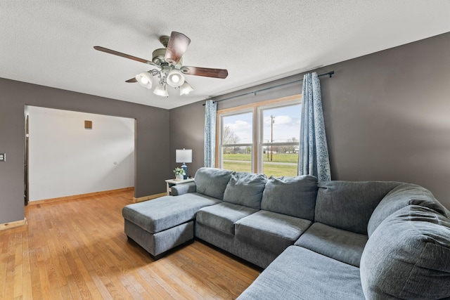 living area with baseboards, light wood-style floors, a textured ceiling, and ceiling fan