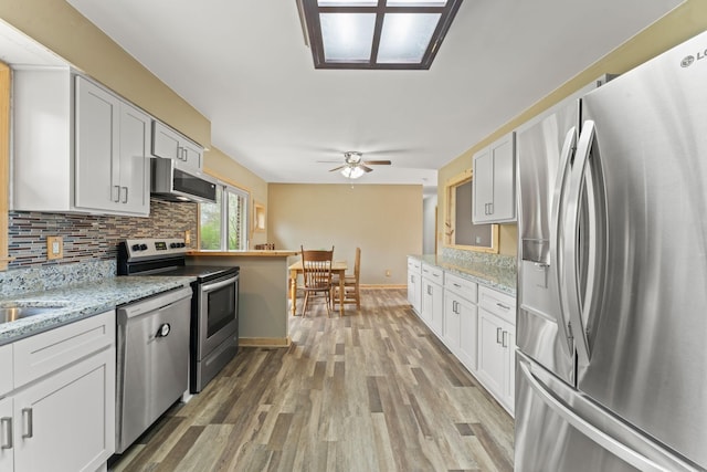 kitchen with white cabinets, stainless steel appliances, a ceiling fan, light wood-type flooring, and backsplash