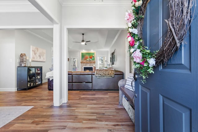 foyer with a lit fireplace, crown molding, a ceiling fan, wood finished floors, and baseboards