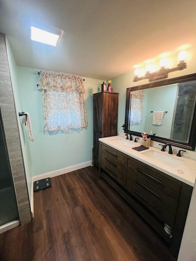 full bathroom with baseboards, double vanity, a sink, and wood finished floors