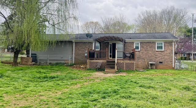 rear view of house with fence, a wooden deck, brick siding, a shingled roof, and a yard