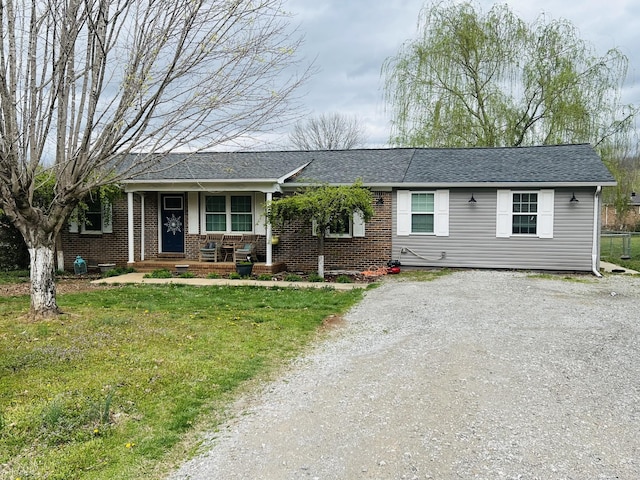 ranch-style house with roof with shingles, driveway, a front yard, brick siding, and a porch