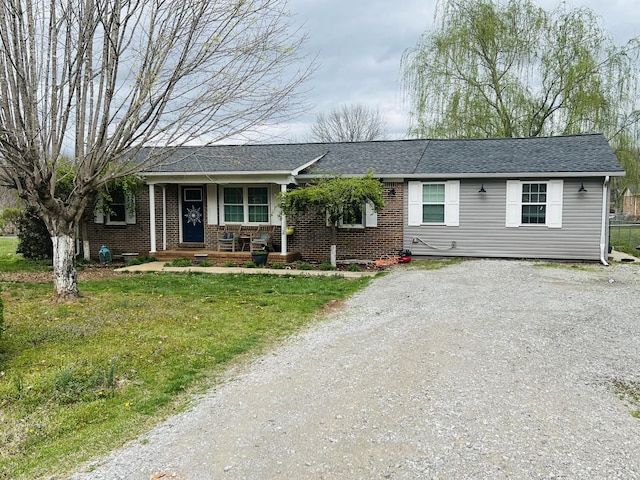 ranch-style house featuring gravel driveway, a front yard, brick siding, a porch, and a shingled roof