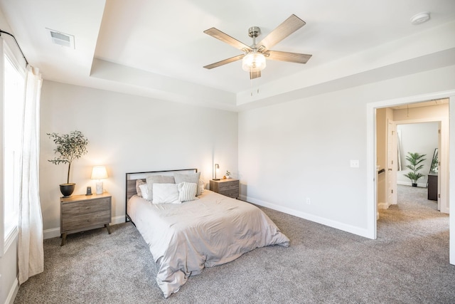 carpeted bedroom featuring a tray ceiling, baseboards, and visible vents