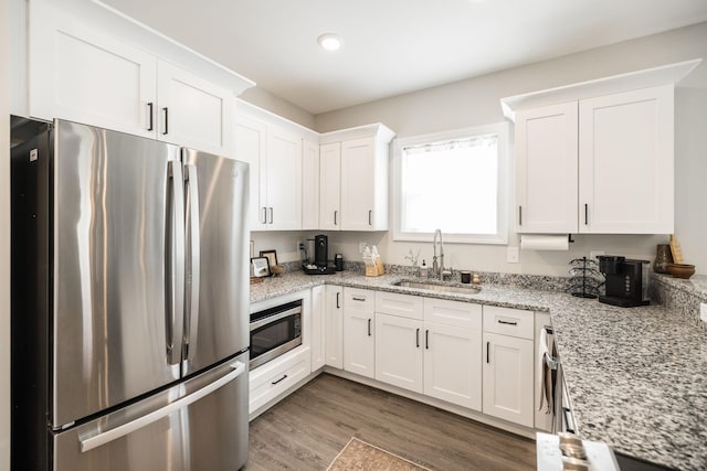 kitchen featuring a sink, light stone counters, white cabinets, appliances with stainless steel finishes, and wood finished floors