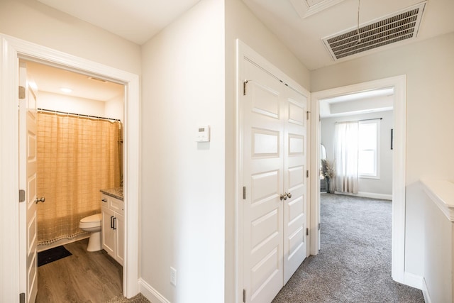 hall featuring baseboards, visible vents, dark wood-type flooring, and dark colored carpet