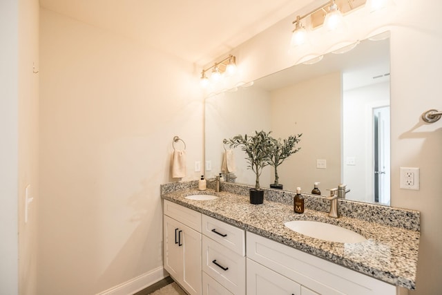 bathroom featuring baseboards, double vanity, visible vents, and a sink