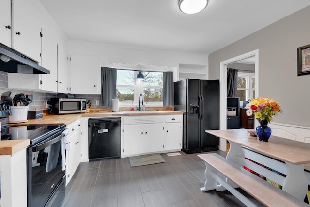 kitchen featuring a sink, under cabinet range hood, black appliances, and plenty of natural light