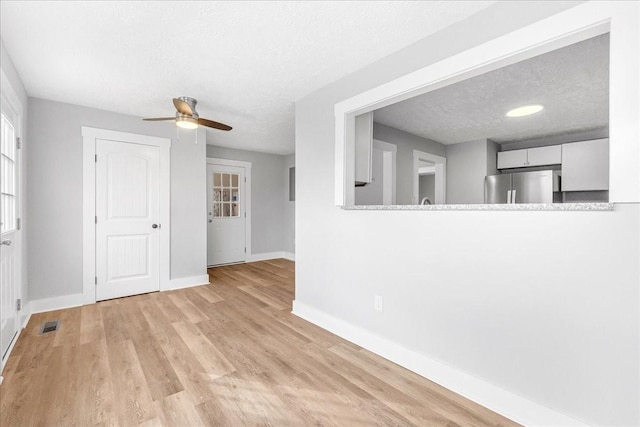 unfurnished living room with a ceiling fan, wood finished floors, baseboards, and a textured ceiling
