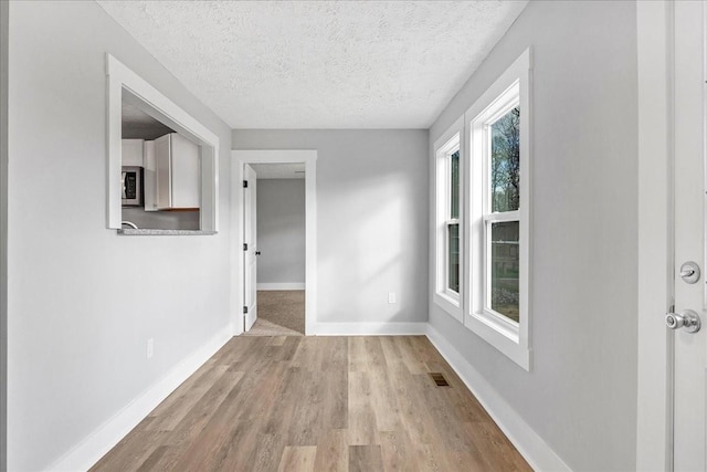 unfurnished room with baseboards, visible vents, light wood-type flooring, and a textured ceiling