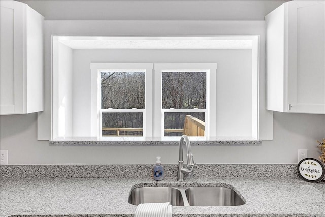 interior details with white cabinets, a sink, and light stone counters
