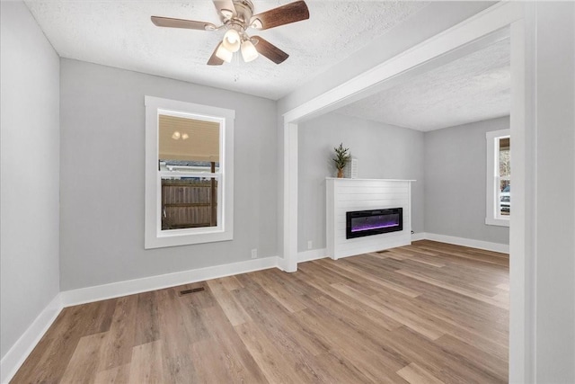 unfurnished living room featuring a textured ceiling, visible vents, baseboards, wood finished floors, and a glass covered fireplace
