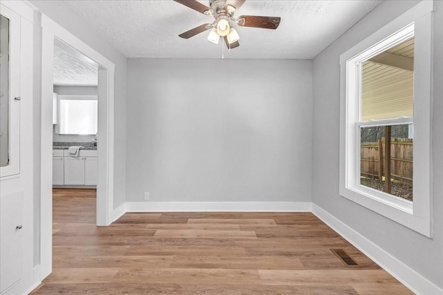 spare room with a ceiling fan, light wood-style flooring, baseboards, and a textured ceiling