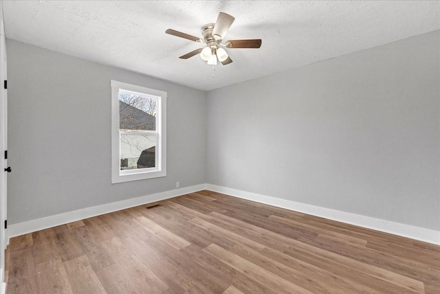 unfurnished room featuring a textured ceiling, light wood-type flooring, baseboards, visible vents, and ceiling fan