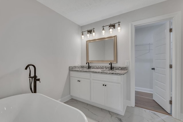 full bathroom with double vanity, a freestanding tub, marble finish floor, and a sink