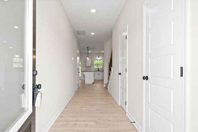 hallway featuring baseboards, light wood-style flooring, visible vents, and recessed lighting