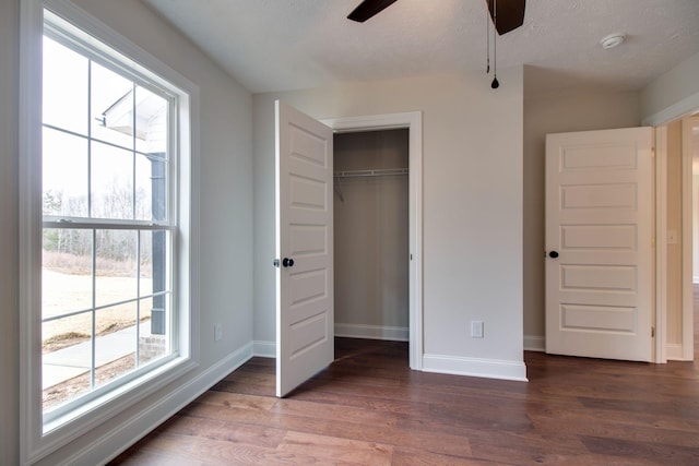 unfurnished bedroom with wood finished floors, a closet, baseboards, and multiple windows
