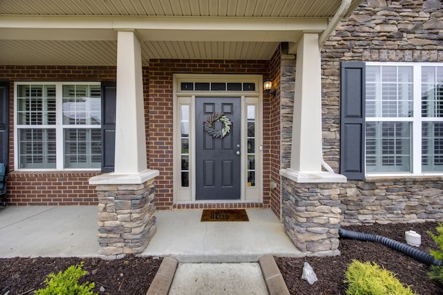 entrance to property featuring brick siding, a porch, and stone siding
