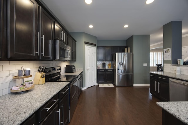 kitchen with light stone countertops, dark wood-type flooring, stainless steel appliances, baseboards, and backsplash