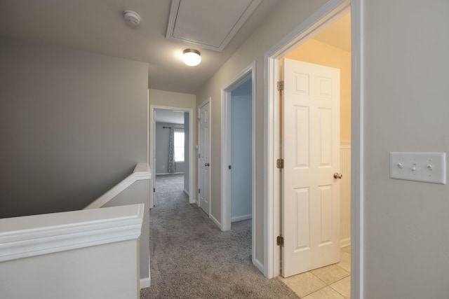 corridor with baseboards, light colored carpet, and attic access